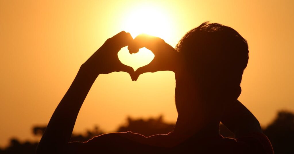 A silhouette of hands forming a heart shape against a vibrant sunset in Bangladesh.