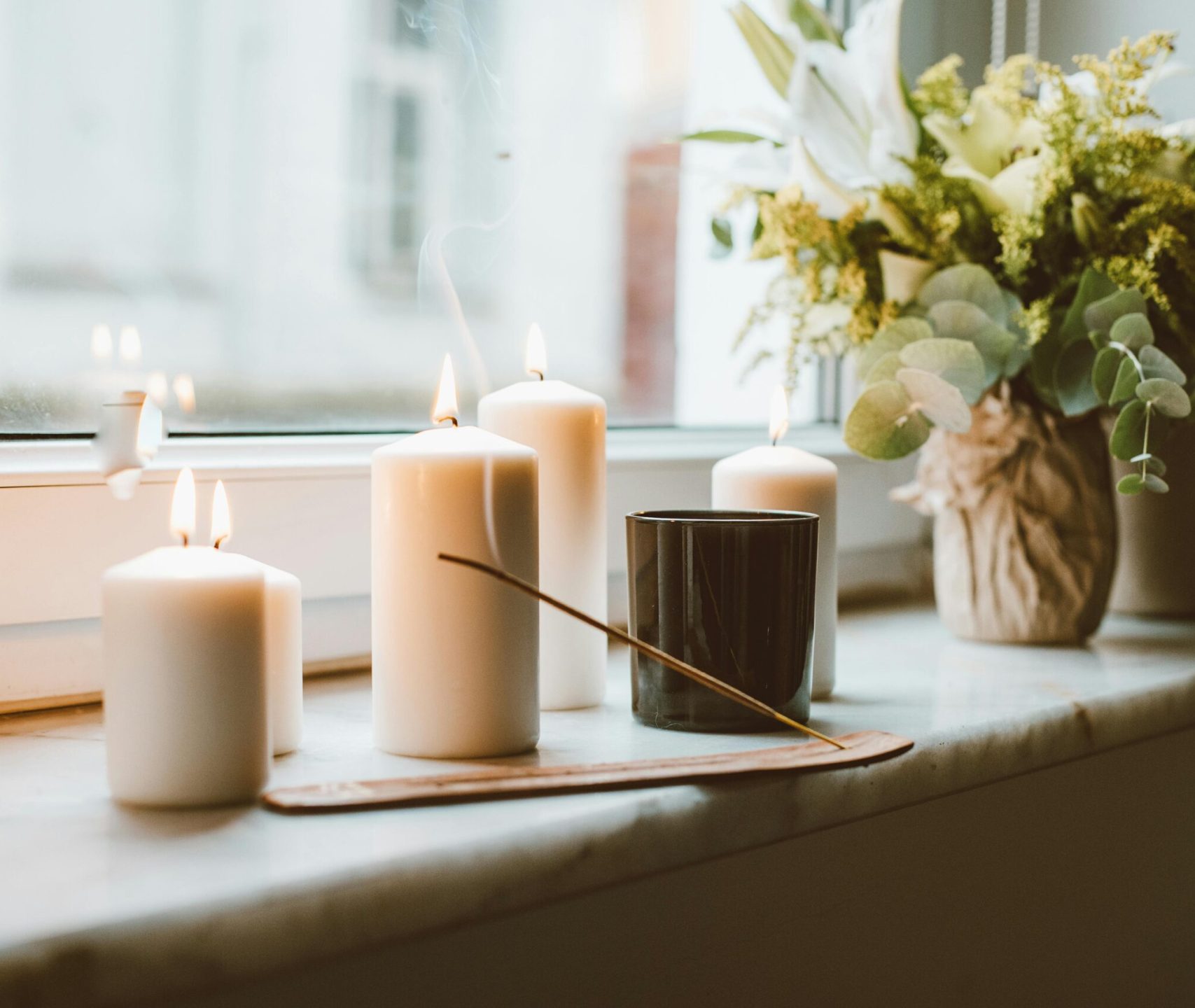 A serene setup of candles and flowers on a window sill, creating a calming atmosphere.